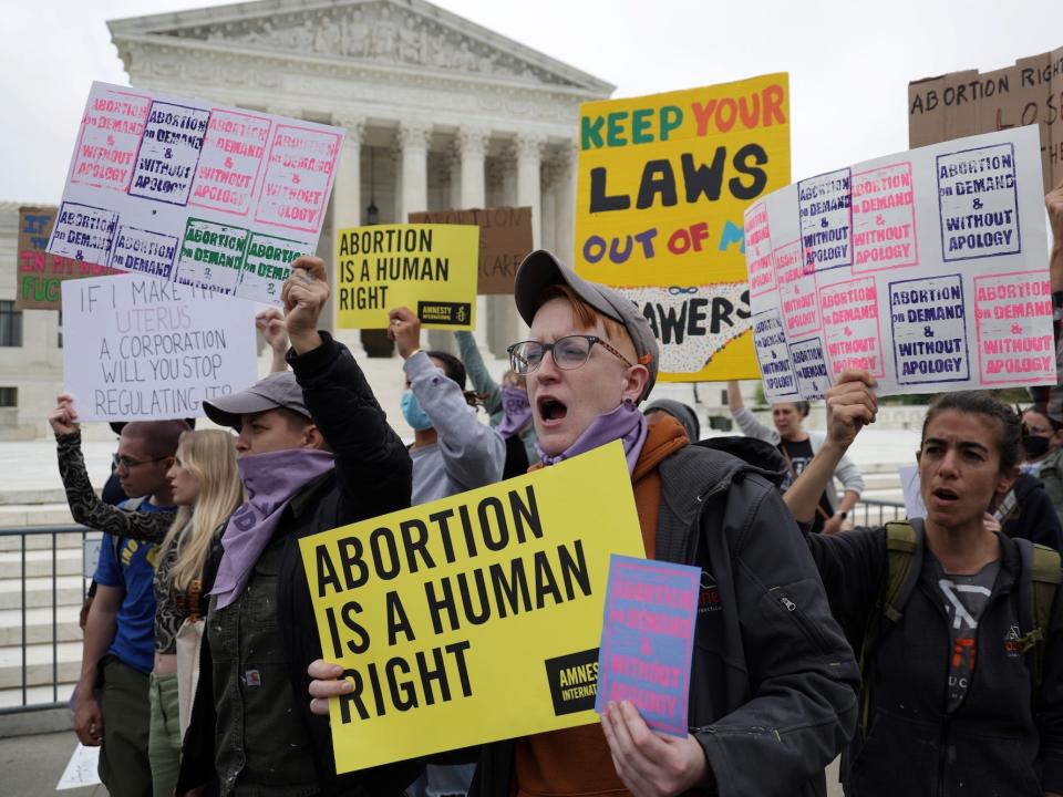 A group of abortion rights activists, some hoisting homemade signs aloft that read "Abortion is a human right." protest the looming reversal of Roe v. Wade on the steps of the Supreme Court.