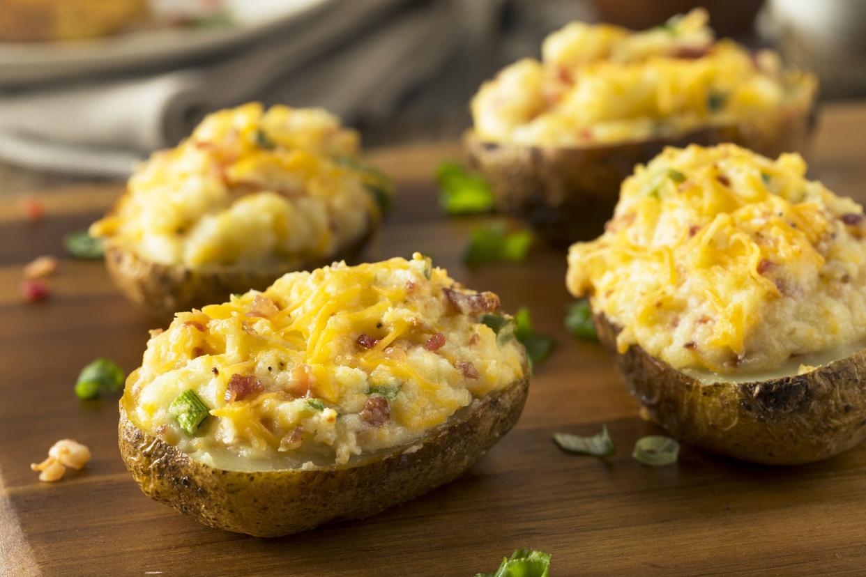 Four loaded potatoes on an artisanal wooden board, selective focus, surrounded by herbs with a blurred background of napkins and another food dish