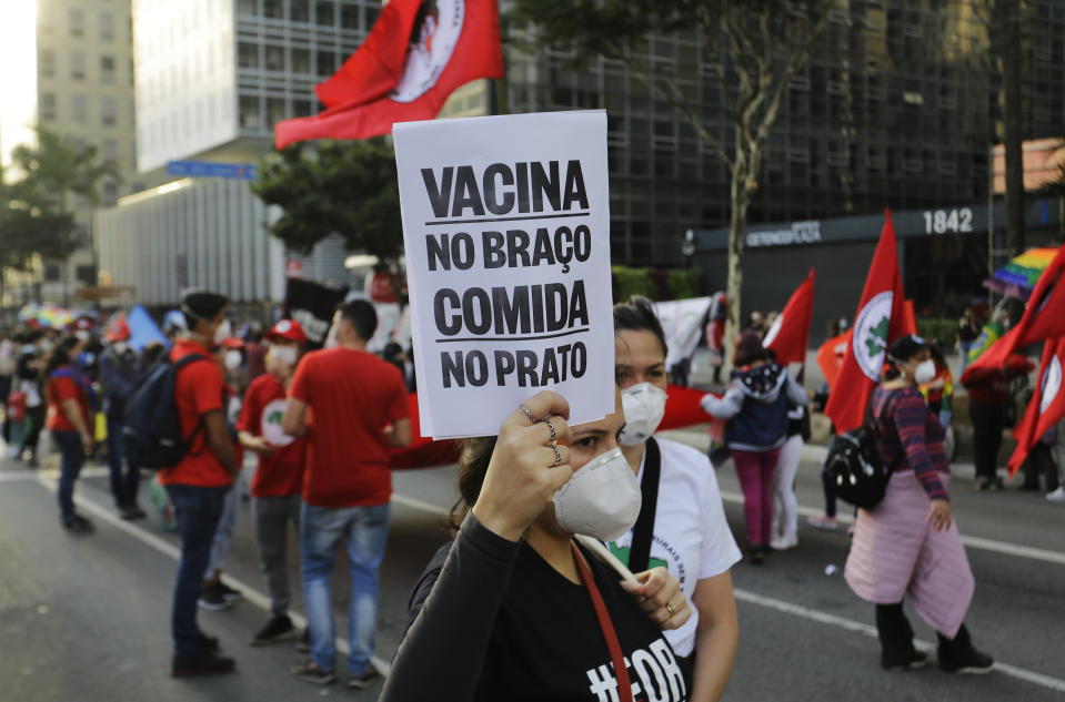 Ademonstrator holds a sign with a message that reads in Portuguese; "Vaccine in the arm, food in the plate" during a protest demanding Bolsonaro resign, in Sao Paulo, Brazil, Saturday, July 3, 2021. Activists called for nationwide demonstrations against Bolsonaro, gathering protestors to demand his impeachment amid allegations of potential corruption in the Health Ministry’s purchase of COVID-19 vaccines. (AP Photo/Nelson Antoine)