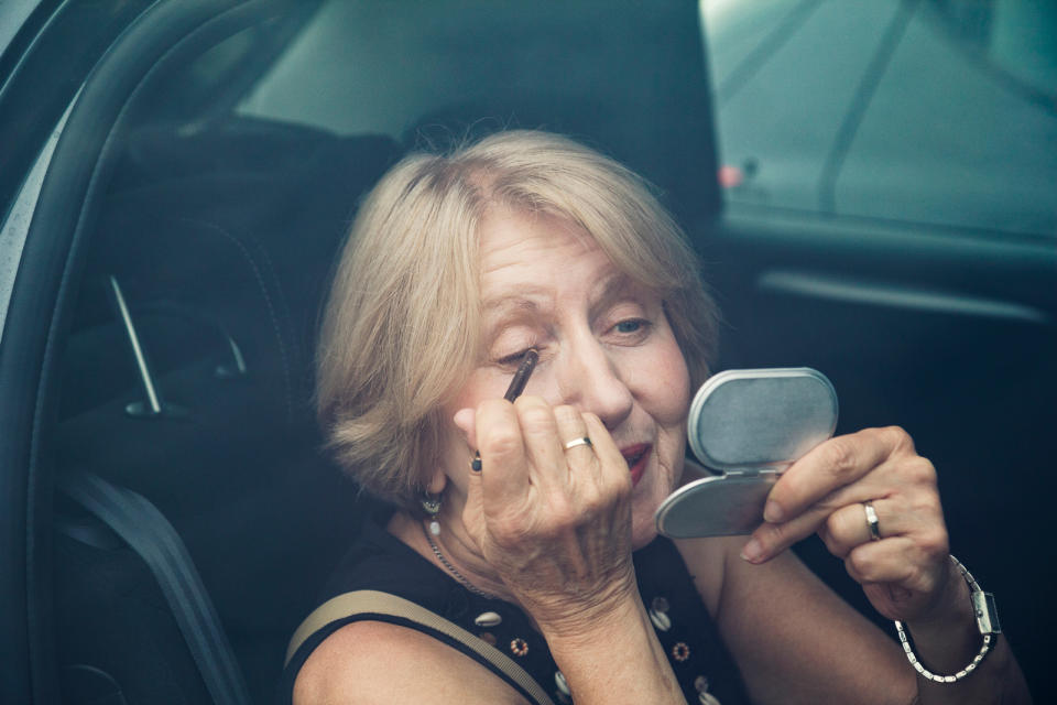 Senior woman applying make up in a car 