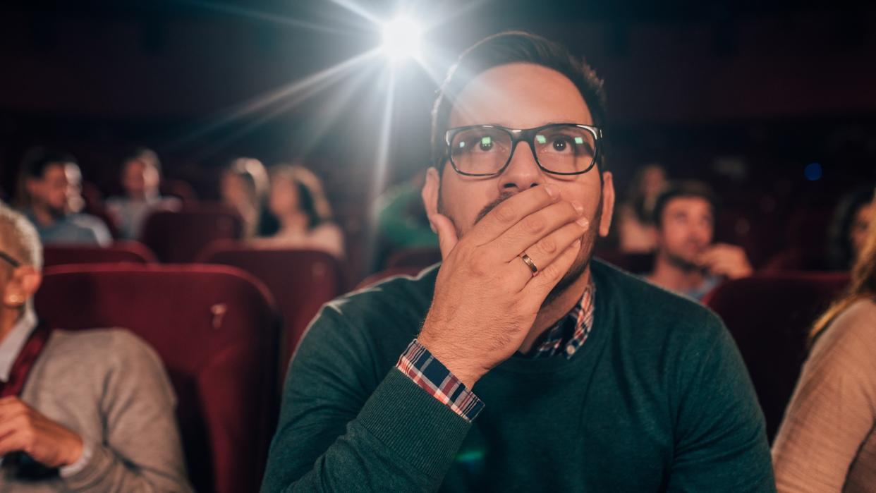 Young man watching a horror movie at the cinema.