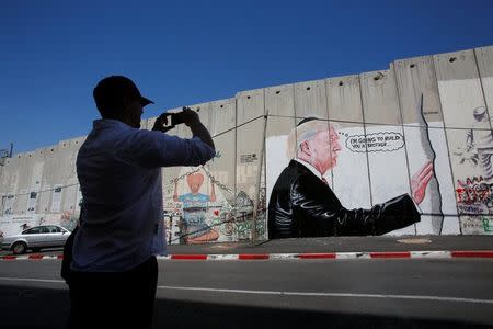 A man takes a photo of a graffiti depicting U.S President Donald Trump on the controversial Israeli barrier in the West Bank town of Bethlehem August 4, 2017. REUTERS/Mussa Qawasma