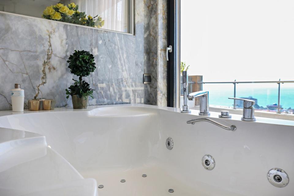 jetted bathtub in corner of bathroom by window with marble wall