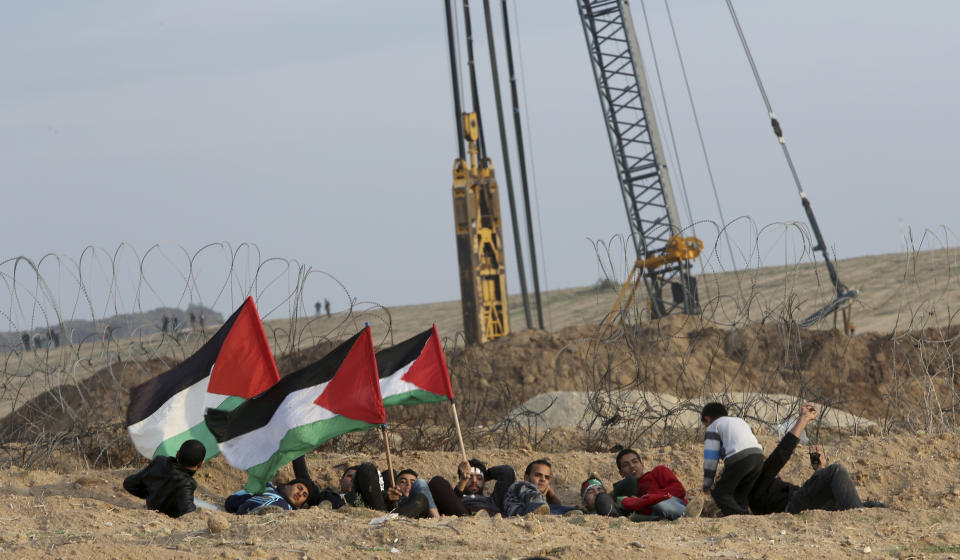 Protesters take cover while waving their national flags near the fence of Gaza Strip border with Israel during a protest east of Gaza City, Friday, Nov. 16, 2018. (AP Photo/Adel Hana)