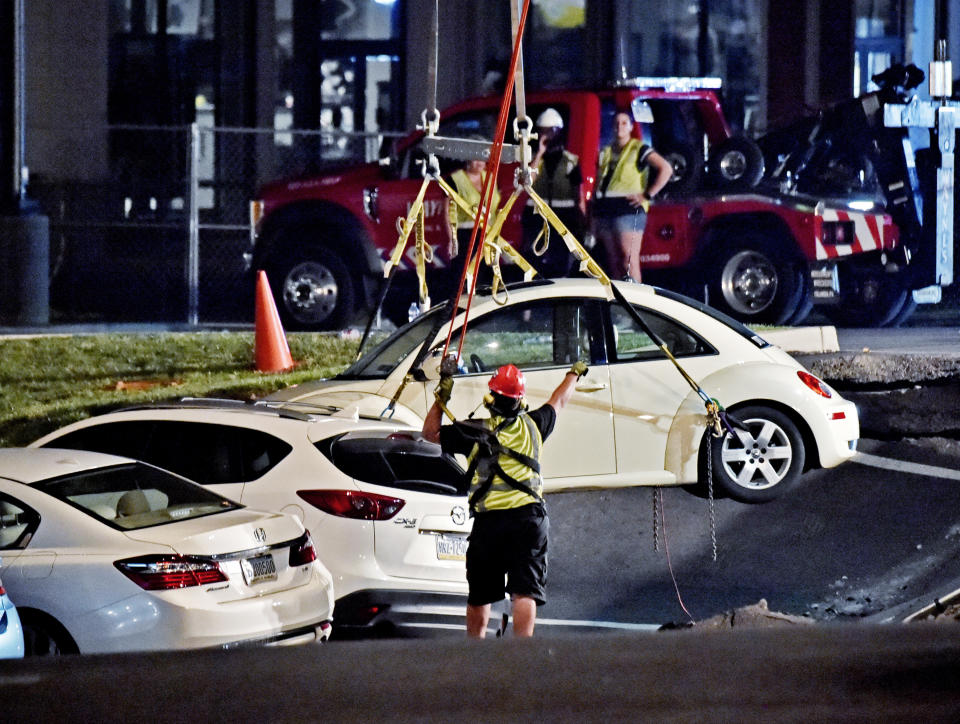 A crane is used to lift vehicles from a sinkhole at Tanger Outlets in Lancaster Pa., shortly after midnight Saturday, Aug. 11, 2018. The sinkhole opened in the parking lot of the outlet Friday afternoon trapping several vehicles. (Blaine Shahan /LNP/LancasterOnline via AP)