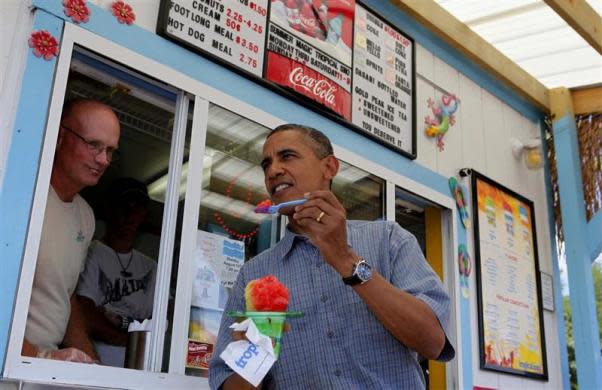 President Barack Obama (R) prepares to eat an ice treat after being served by owner Steve Holt at Tropical Sno in Denison, Iowa, while touring the state in a bus, August 13, 2012.