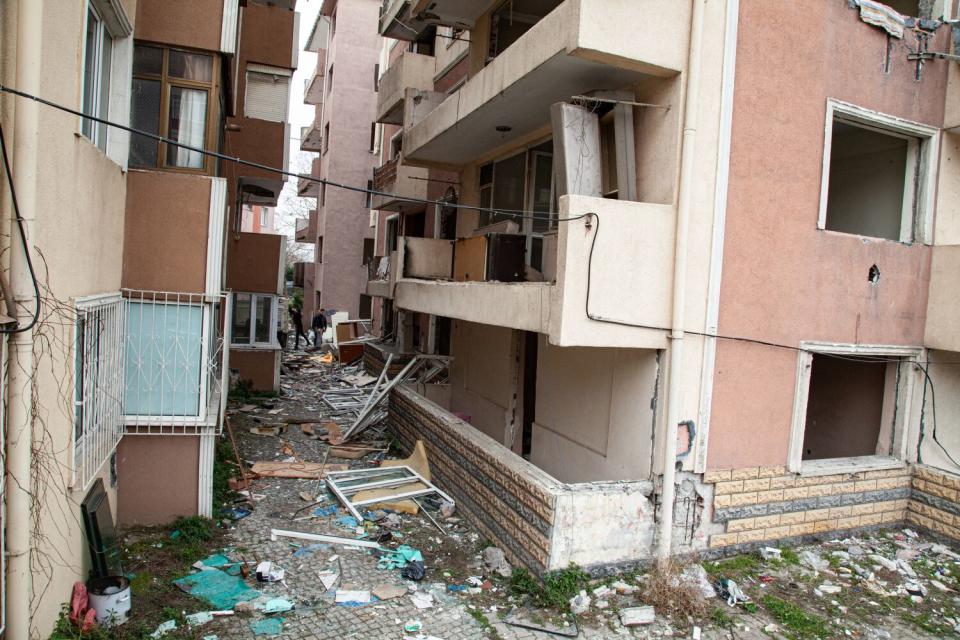 A view of beige-, brown- and peach-colored apartments with missing windows and debris on the ground