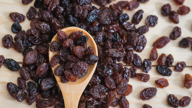 Raisins on a wooden table with some in a wooden spoon