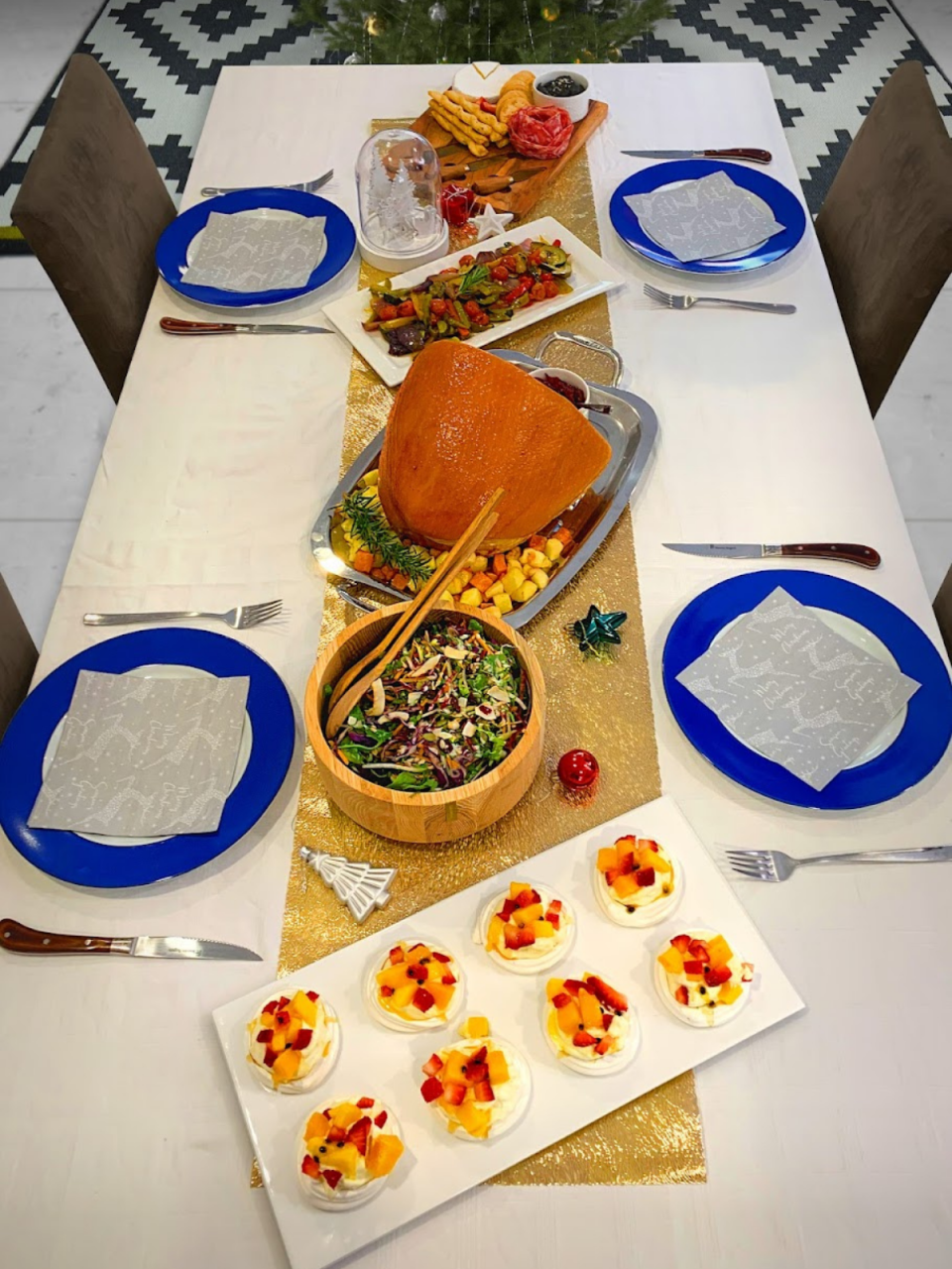 A dining table set for four places with ham, meringues and salad.