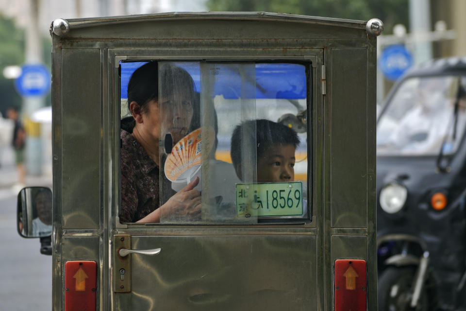 A woman cools herself with a fan as she rides a tricycle with a child on a hot day in Beijing, Monday, July 3, 2023. Heavy flooding has displaced thousands of people around China as the capital had a brief respite from sweltering heat. Beijing reported 9.8 straight days when the temperature exceeded 35 C (95 F), the National Climate Center said Monday. (AP Photo/Andy Wong)