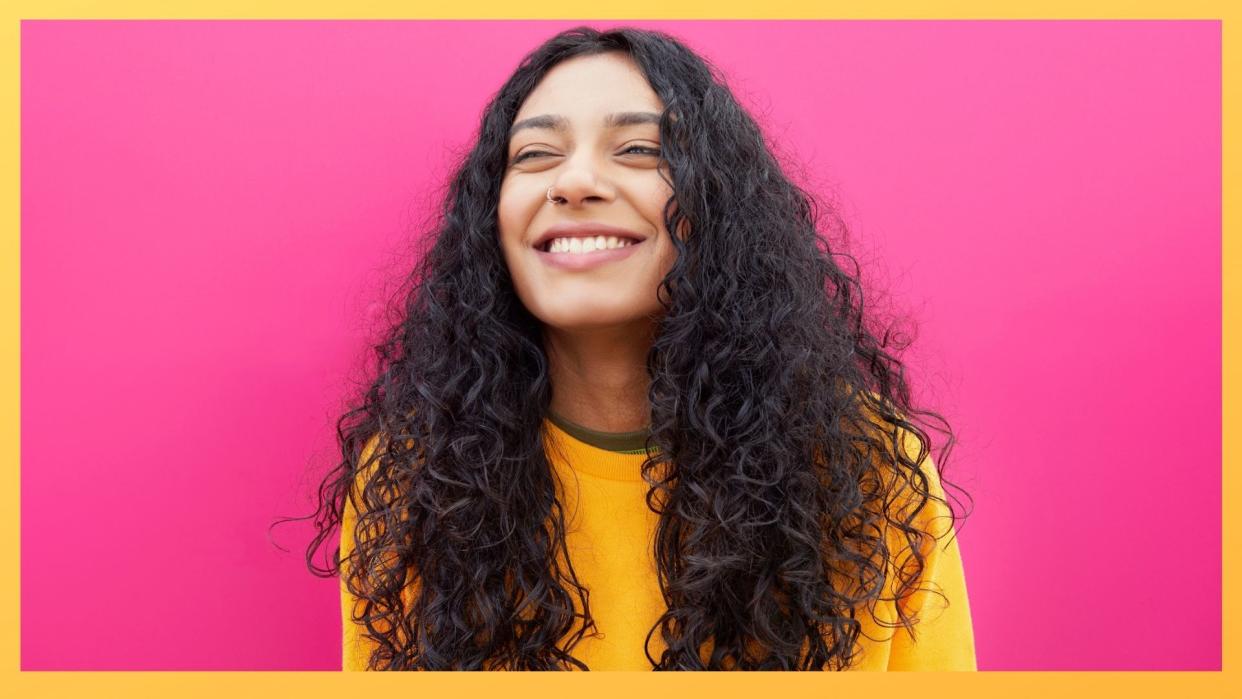 A girl with curly hair in a yellow jumper on a pink and yellow background for the curly girl method article 