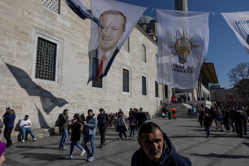 FILE PHOTO: People walk under election posters for Turkey's President Tayyip Erdogan and his ruling AK Party flags in Istanbul