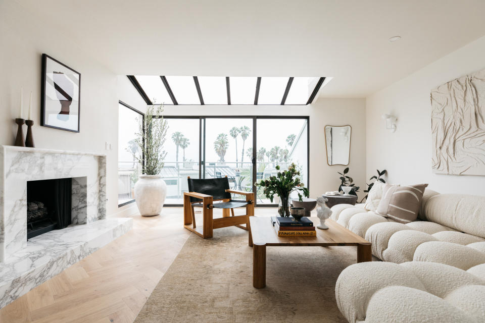 A neutral living room with herringbone flooring, a boucle sofa, and a marble fireplace