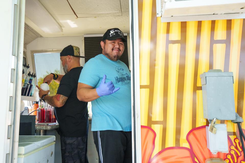 Owner, Desmond Martin, left, works as his son, Anthony Martin, right, turns toward the camera in the Happy Honu Shave Ice truck on April 16, 2022, at the Arrowhead Farmers Market in Glendale, Ariz.