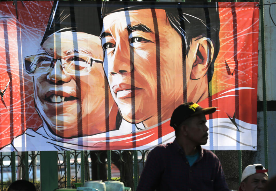 A man sits near banner of Indonesian President Joko Widodo and his deputy Ma'ruf Amin in Jakarta, Indonesia, Sunday, Oct. 20, 2019. Indonesian President Joko Widodo, who rose from poverty and pledged to champion democracy, fight entrenched corruption and modernise the world's most populous Muslim-majority nation, was sworn in Sunday for his second and final five-year term with a pledge to take bolder actions. (AP Photo/Tatan Syuflana)