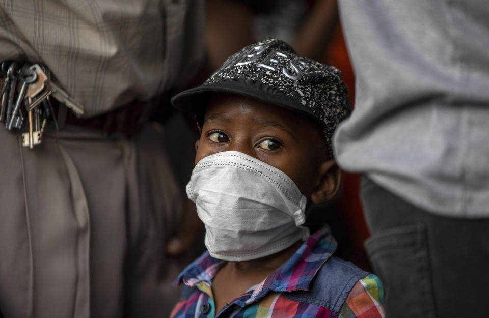 A young boy wearing a face mask to protect against coronavirus, with his father stands in a queue to shop in Soweto, South Africa, Thursday, March 26, 2020. In hours South Africa goes into a nationwide lockdown for 21-days in an effort to mitigate the spread to the coronavirus. (AP Photo/Themba Hadebe)