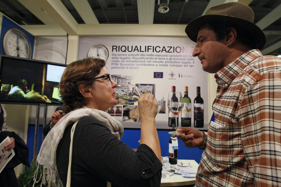 Marcio Alexandre Alberto, a Brazilian sommelier, right, is flanked by an unidentified woman tasting a glass of white wine in a 'Pon sicurezza project' stand at the 46th edition of the annual International Wine and Spirits Exhibition "Vinitaly", in Verona, northern Italy, Monday, March 26, 2012. The wine exhibition runs until March 28. (AP Photo/Luca Bruno)