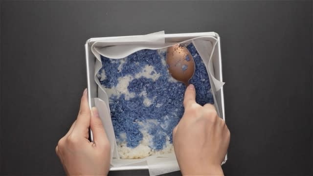 Compressing rice into baking tin with a spoon