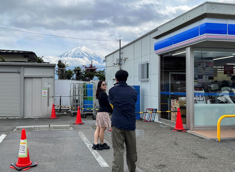 A tourist tries to take photos of Mount Fuji appearing in the background of a convenience store in Fujikawaguchiko town