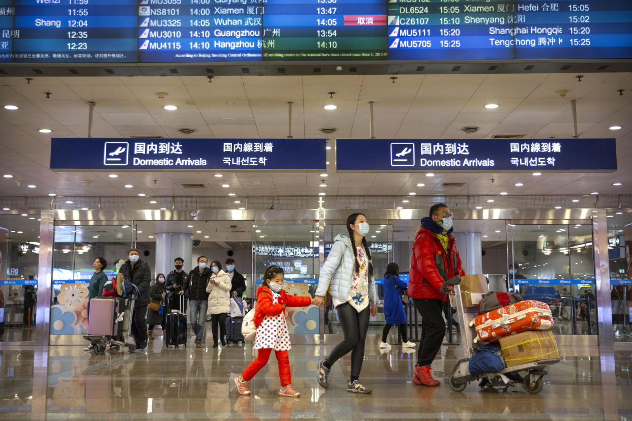 Travelers in face masks walk past a display board showing a canceled flight from Wuhan at Beijing Capital International Airport in Beijing, Thursday, Jan. 23, 2020. China closed off a city of more than 11 million people Thursday, halting transportation and warning against public gatherings, to try to stop the spread of a deadly new virus that has sickened hundreds and spread to other cities and countries in the Lunar New Year travel rush. (AP Photo/Mark Schiefelbein)