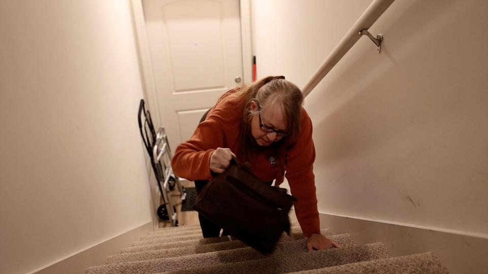 Lisa Vollmer crawls up the stairs to her 2nd floor apartment moving her purse up ahead of her. She keeps a walker at the top and another at the bottom because she can't take it up and down with her.