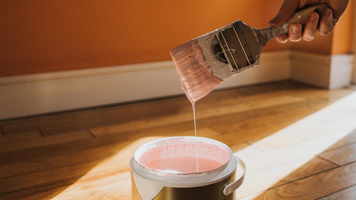 A hand dipping a paint brush into a tin paint