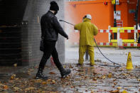 A man walks past a worker removing graffiti from a wall in London, Tuesday, Oct. 27, 2020. The British government is sticking to its strategy of tiered, regional restrictions to combat COVID-19 amid mounting political and scientific pressure for stronger nationwide measures to prevent the pandemic from spiralling out of control. (AP Photo/Kirsty Wigglesworth)