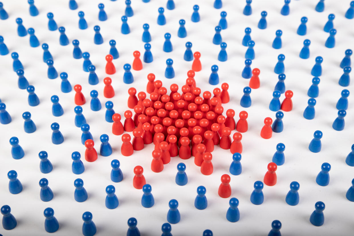 wooden figurines sympolizing covid-19 virus and not infected people around the virus. red figurines are the superspreader and the blue ones are safe because of the distance, white background