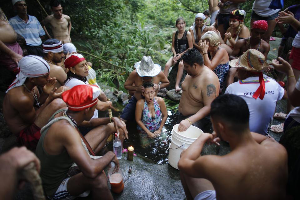 In this photo taken Oct. 12, 2019, Juan Carlos Paso performs a cleansing ritual on a woman in a pool of water on Sorte Mountain where followers of indigenous goddess Maria Lionza gather annually in Venezuela's Yaracuy state. Devotees say the number of followers swells as Venezuelans turn for answers to the struggle of daily life outside traditional political system, churches and hospitals. (AP Photo/Ariana Cubillos)