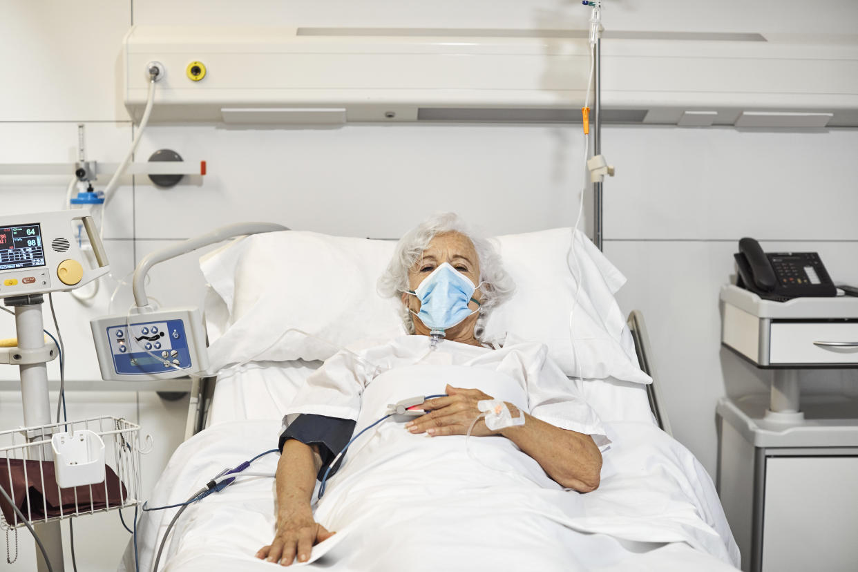 Portrait of senior woman with oxygen mask lying on bed. Elderly female patient is in intensive care unit during COVID-19. She is in hospital ward.