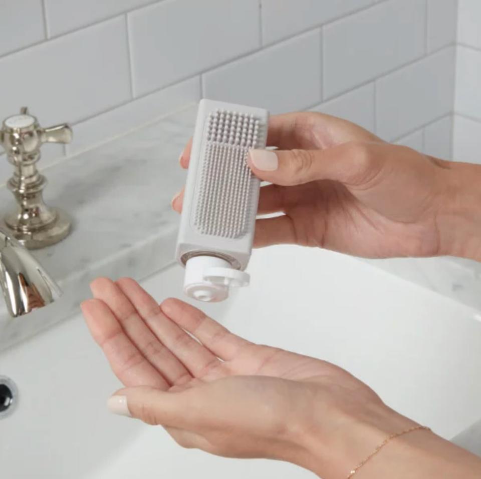 a model holding the grey bottle with a textured side above a sink