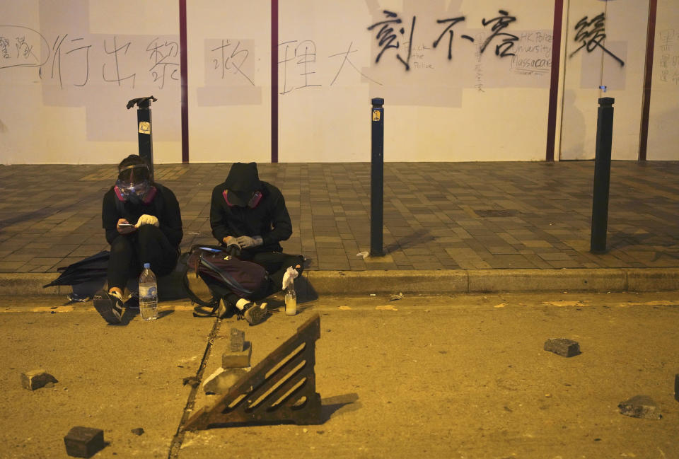 Protestors rest near a road barricaded with bricks in Hong Kong, early Tuesday, Nov. 19, 2019. About 100 anti-government protesters remained holed up at a Hong Kong university Tuesday as a police siege of the campus entered its third day. (AP Photo/Vincent Yu)