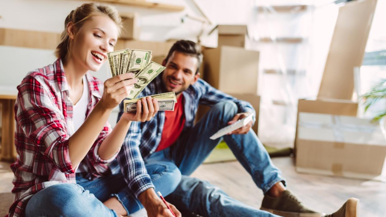 happy young couple with calculator and dollar banknotes counting money in new apartment.