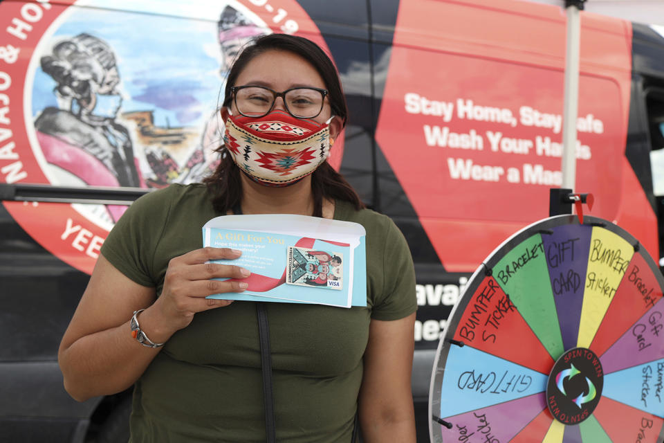 In this photo provided by The Navajo & Hopi Families COVID-19 Relief Fund, Natasha Goldtooth shows off a $25 gift certificate she won after spinning a prize wheel for people who are fully vaccinated on Aug. 21, 2021, in Window Rock, Ariz. Initially, the campaign began at local area flea markets and vaccination sites before becoming primarily virtual. Arizona is the only state where rural vaccine rates outpaced more populated counties according to a recent report from the U.S. Centers for Disease Control and Prevention. Public health experts believe the unexpected trend was mainly fueled by a group that lost a disproportionate number of lives to COVID-19: Native Americans. (Mihio Manus/The Navajo & Hopi Families COVID-19 Relief Fund via AP)