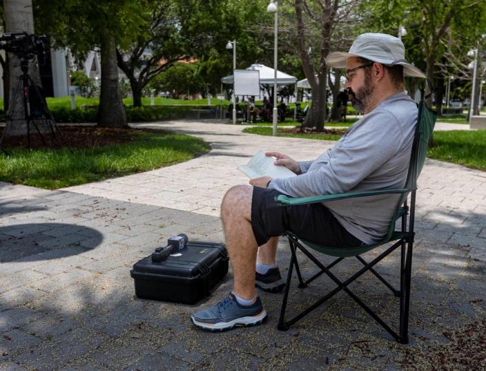 Orlando Montejo, cameraman for WSVN, Channel 7, Miami, reads a book in the shade of a palm tree outside the Federal Courthouse in Miami as a grand jury collects evidence related to the possible mishandling of classified documents by former President Donald J. .Trump.
