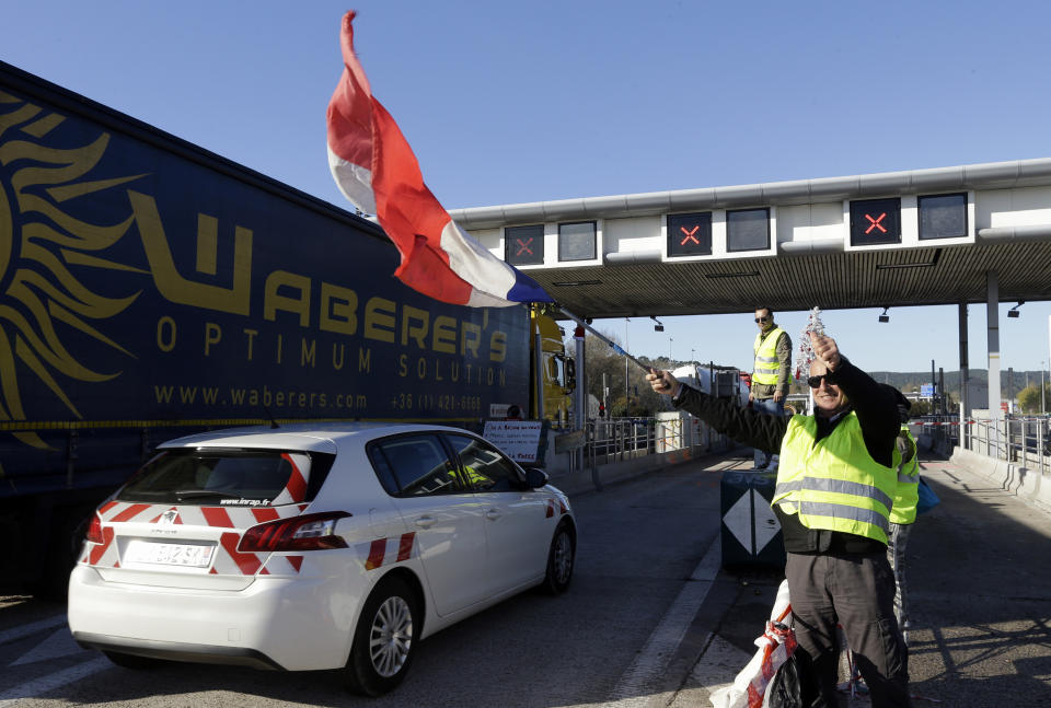 A demonstrators wearing a yellow vest waves a French flag as demonstrators open the toll gates on a motorway near Aix-en-Provence, southeastern France, Tuesday, Dec. 4, 2018. French Prime Minister Edouard Philippe announced a suspension of fuel tax hikes Tuesday, a major U-turn in an effort to appease a protest movement that has radicalized and plunged Paris into chaos last weekend. (AP Photo/Claude Paris)