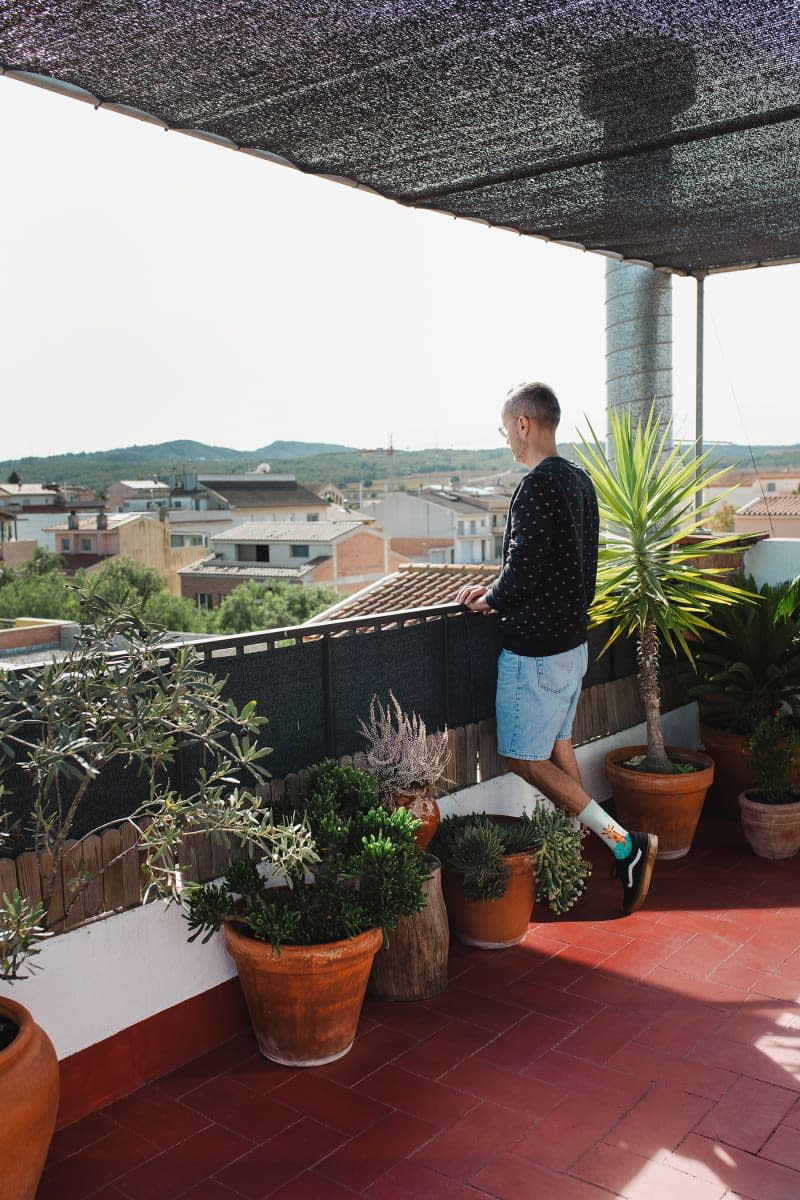 Dweller standing on plant filled terra cotta balcony.
