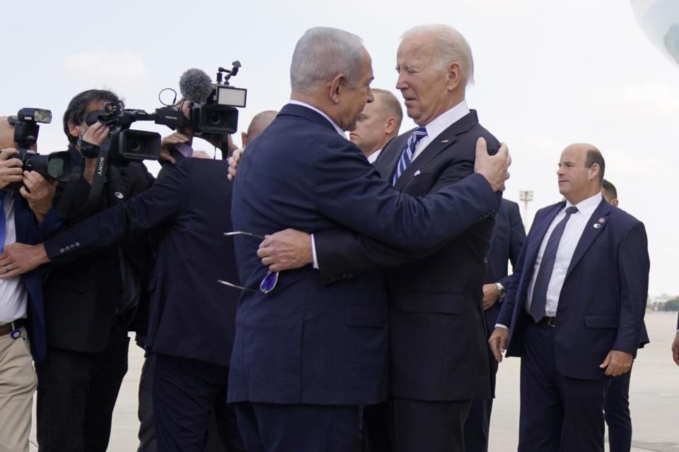 Two men in dark suits embrace near photographers