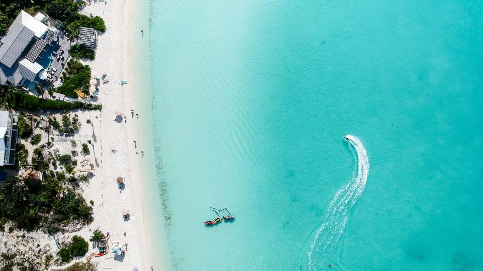 Drone photo of beach in Grace Bay, Providenciales, Turks and Caicos. The caribbean blue sea and underwater rocks can be seen, as well as some jet skies