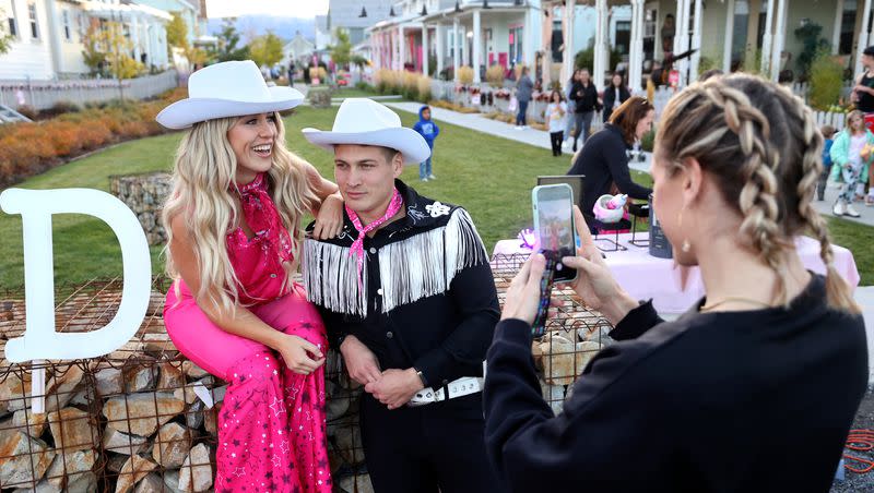 Chloe Ford, right, takes a photo of Sidney Ford and Chris Gerac, dressed as Barbie and Ken, in a Daybreak neighborhood that is decorated in a “Barbie” theme for Halloween in South Jordan on Friday, Oct. 13, 2023.