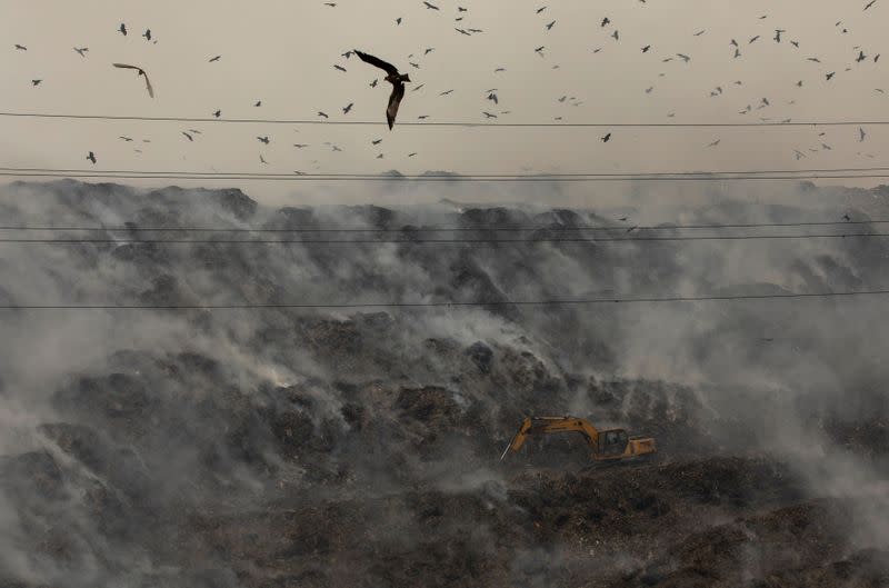 An excavator tries to contain the fire as smoke billows from burning garbage at the Ghazipur landfill site in New Delhi