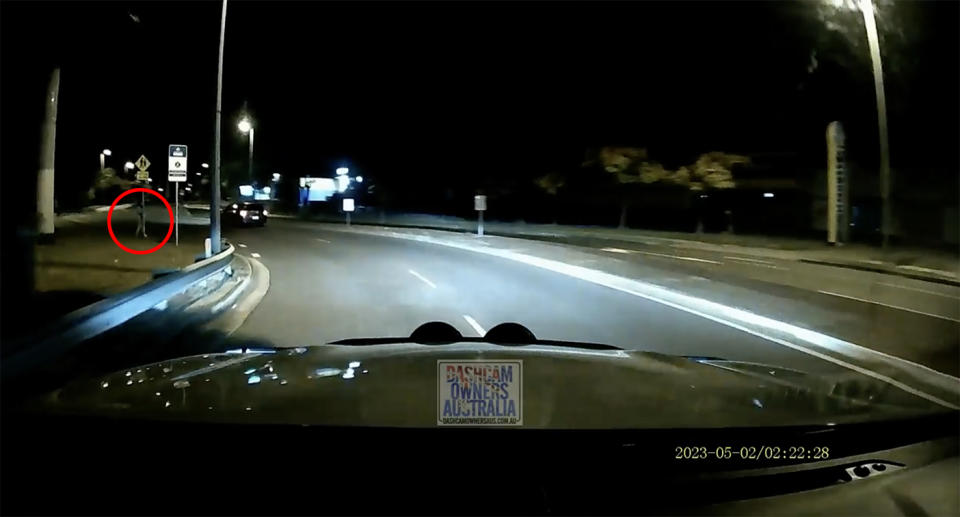 A woman can be seen standing behind a sign next to Grand Plaza Drive in Browns Plains.