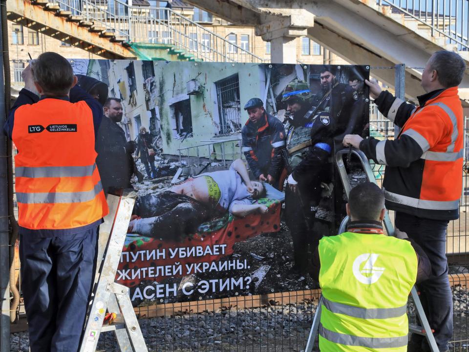 Workers attach a banner with a photo of a pregnant woman being carried on a stretcher after the bombing of a maternity ward in Mariupol during Russia's war in Ukraine that is displayed as part of an exhibition at the railway station in Vilnius, Lithuania