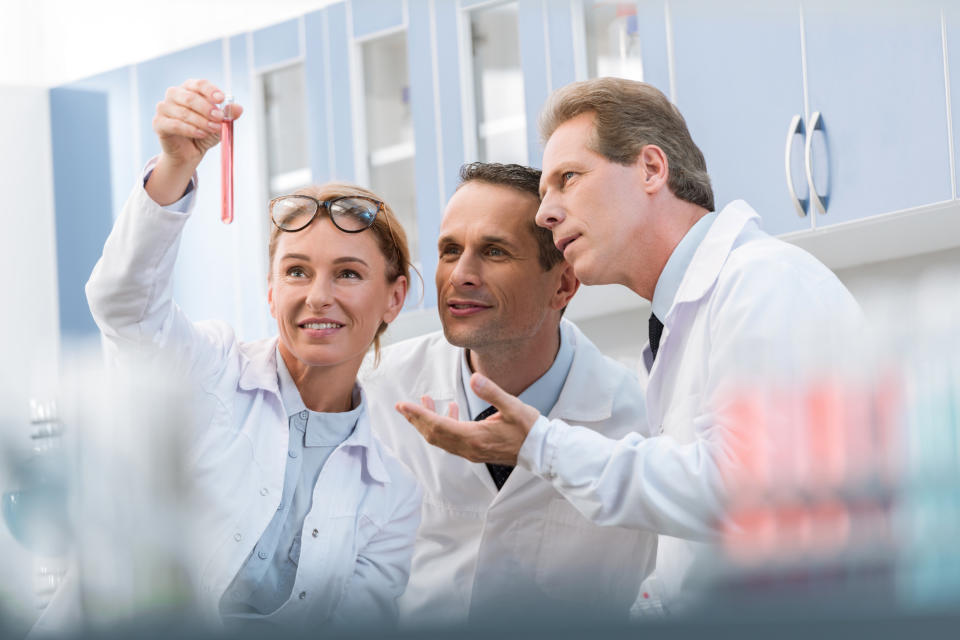 Three scientists discussing a pink test tube.