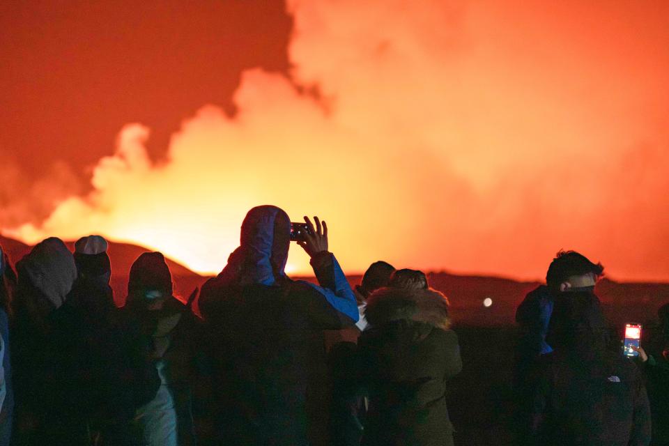 People gather to watch as molten lava flows out from a fissure on the Reykjanes peninsula north of the evacuated town of Grindavik, western Iceland on March 16, 2024. Lava spewed Saturday from a new volcanic fissure on Iceland's Reykjanes peninsula, the fourth eruption to hit the area since December, authorities said.