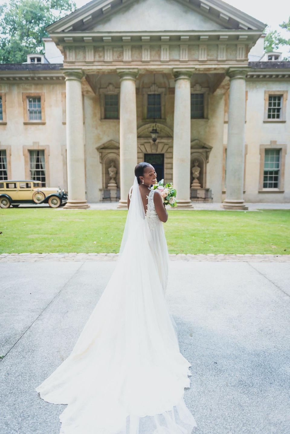 A bride looks over her shoulder while posing in front of a mansion.