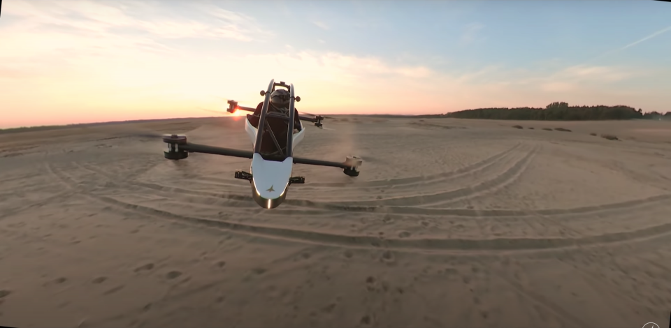 A Jetson One all-electric personal aircraft hovering over a sandy beach at sunset.