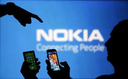 Men are silhouetted against a video screen with a Nokia logo as he poses with Nokia Lumia 820 and Samsung S4 smartphones in this photo illustration taken in the central Bosnian town of Zenica, August 14, 2013. REUTERS/Dado Ruvic