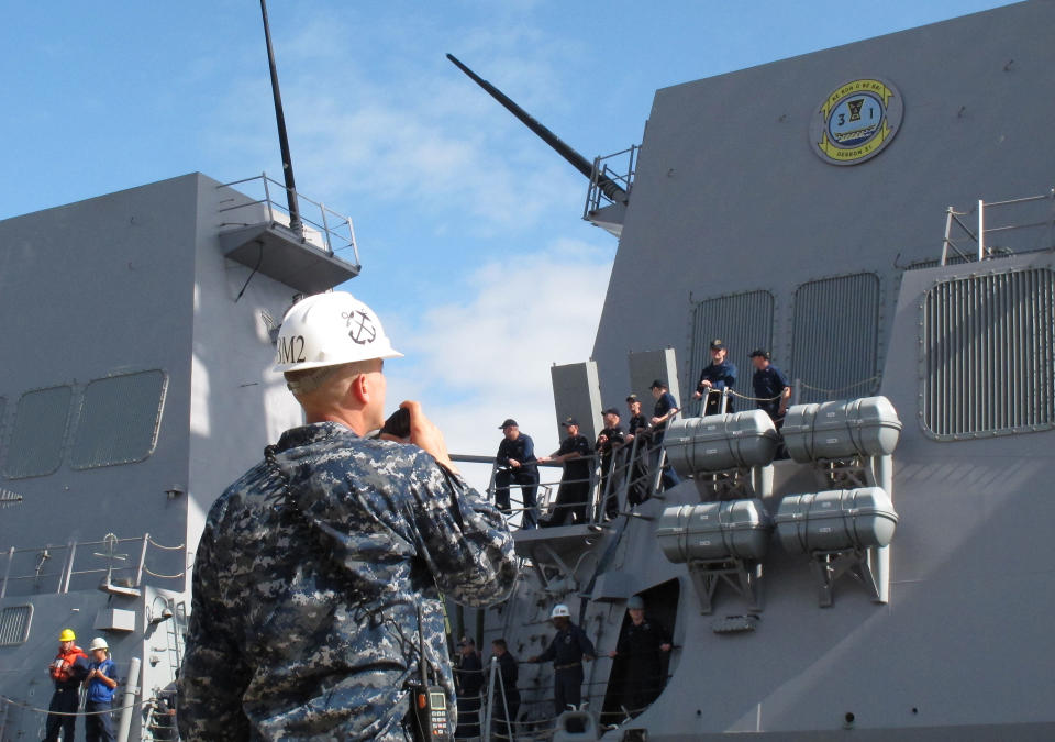 A dock worker watches as American naval destroyer USS Michael Murphy escorts passengers from a Canadian navy vessel to Pearl Harbor, Hawaii, Tuesday, March 4, 2014. A U.S. Navy ocean tug was towing the Canadian ship after an engine fire left 20 sailors with minor injuries. (AP Photo/Oskar Garcia)