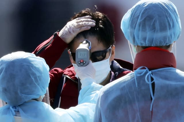 An official in a protective suit takes the temperature of a passenger disembarking from the quarantined Diamond Princess cruise ship in Yokohama, near Tokyo 